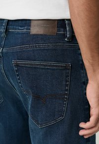 Dunkelblaue Jeans aus Denim mit einem Lederetikett "DENIM SUPPLY", kontrastierenden Nähten und einer Gesäßtasche mit einer geschwungenen Nahtdetails.