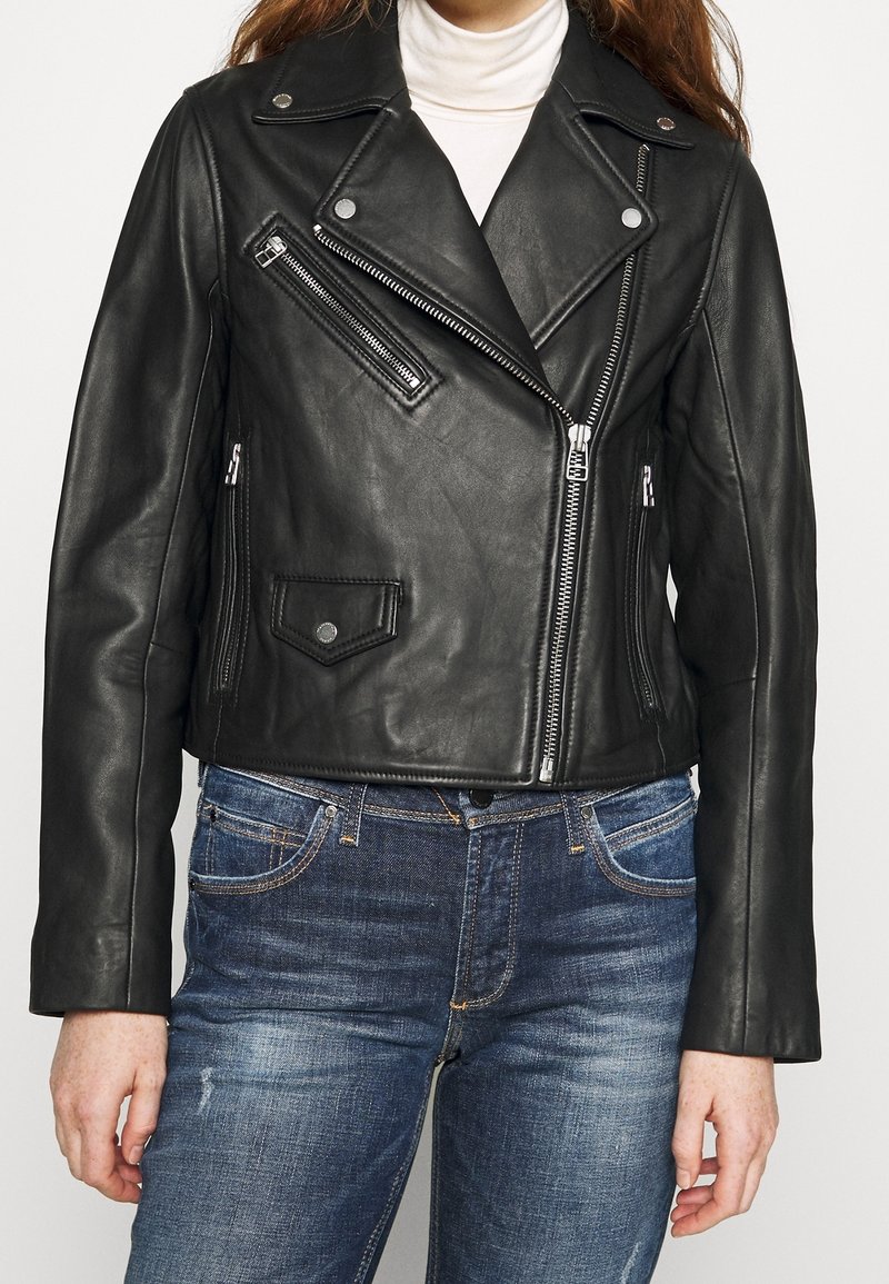 Černá kožená motorkářská bunda se stříbrnými zipy a patentkami, s přiléhavým střihem a krátkou délkou, kombinovaná s modrými džíny.