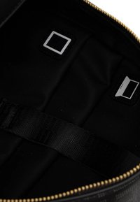 Interior de bolsa de tela negra, con cierre de cremallera y herrajes en tono dorado, dos uniones cuadradas y una correa texturizada.