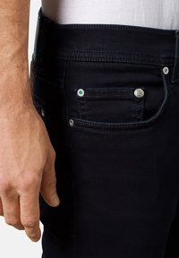 Jeans de denim oscuro con un ajuste slim, que presentan herrajes plateados, un botón verde como detalle y un bolsillo en el lateral.