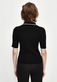 Top en maille côtelée noire avec un col blanc et un bord de manche blanc. Manches courtes, coupe ajustée et texture lisse.