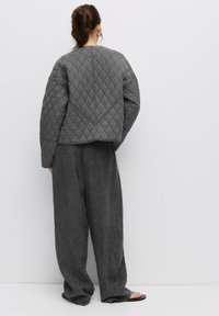 Prošívaná šedá bunda s krátkým střih, široké texturované kalhoty ve stejné šedé barvě, nabízející volný střih a minimalistický styl.
