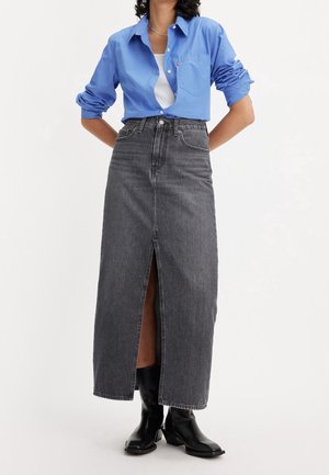 Maxinederdel i mørkegrå denim med frontslids, kombineret med en blå skjorte med knapper og sorte ankelstøvler. Elegant design med synlige teksturdetaljer.