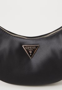 Svart sateng skulderveske med buet design, med glidelås i gulltone og et trekantet logo med "GUESS USA" i preget skrift.