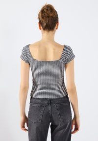 Black and white checkered top with short sleeves and square neckline, paired with high-waisted dark jeans, viewed from the back.