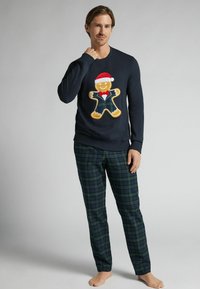 Námořnická mikina s grafikou perníkového muže v obleku a s vánoční čepicí, doplněná zelenými a námořnickými kostkovanými kalhotami. Měkká tkanina, volný střih.