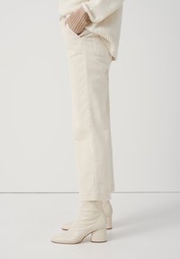 Krämfärgade kordbyxor med rak skärning, bärs med beige läderankelstövlar med klack. Mjuk textur och subtila ribbor synliga.
