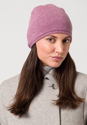 Roze gebreide beanie met een snug fit, gemaakt van zachte wol, met een gestructureerd ribpatroon. Draagt een persoon met steil donker haar.