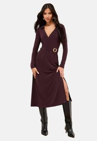Rochie cu mâneci lungi, de culoare burgundă închisă, având guler, talie cu belt și un accent circular, precum și o fante deasupra coapsei. Purtați cu cizme negre până la genunchi.