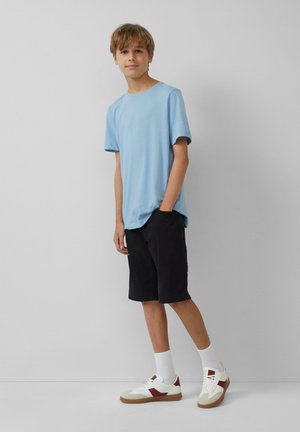 T-shirt di cotone azzurro chiaro, pantaloni corti neri e sneaker bianche con accenti rossi. Design semplice, vestibilità comoda e texture uniformi.
