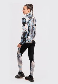 Chaqueta multicolor con cuello alto y patrón abstracto, combinada con leggins negros que presentan un patrón similar, usados con zapatos deportivos.