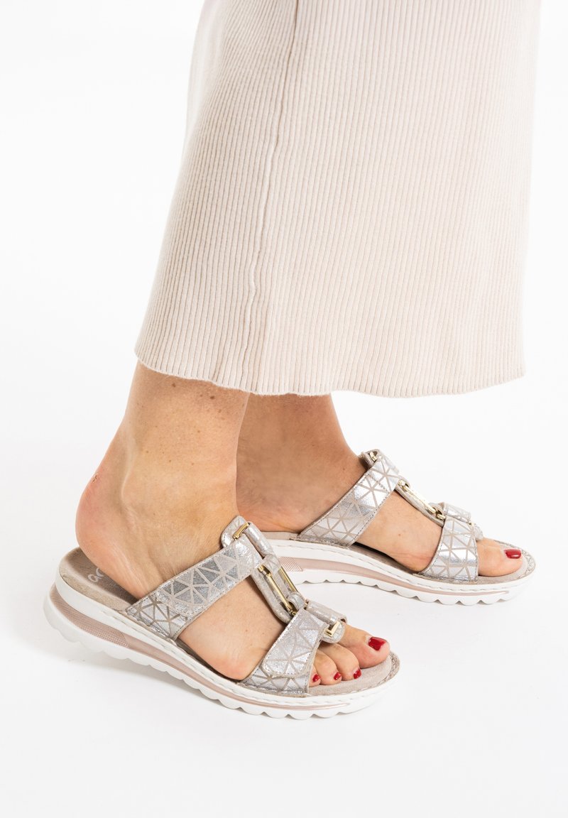 Metaalachtige zilveren sandalen met gekruiste banden, geometrisch patroon en gouden hardware accenten. Gevoerde witte zool voor comfort.