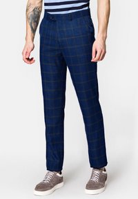 Granatowe spodnie w kratę z teksturowanej tkaniny, o wąskim kroju i pojedynczym zapięciem na guzik, w zestawie z casualowymi szarymi sneakersami.