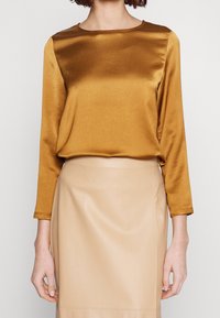Langærmet top i rig sennepsfarvet satin med runde halsudskæring, parret med en beige, glat tekstureret nederdel med en tætsiddende silhuet.