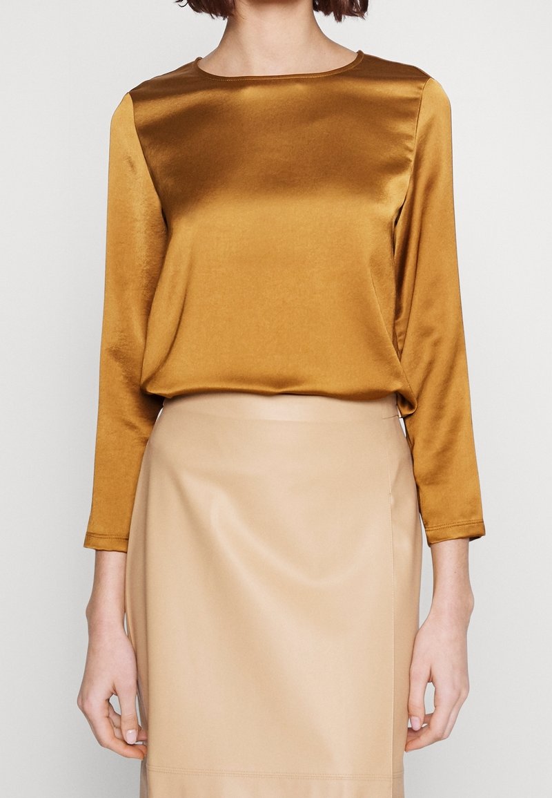 Langærmet top i rig sennepsfarvet satin med runde halsudskæring, parret med en beige, glat tekstureret nederdel med en tætsiddende silhuet.