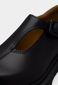 Μαύρο δερμάτινο παπούτσι Mary Jane με λουράκι σε σχήμα Τ και πόρπη, με λείο φινίρισμα και ταμπά εσωτερική επένδυση, εμφανίζεται σε κοντινή λήψη.