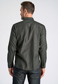 Camisa de manga larga verde oscuro con cuello abotonado, yugo trasero y puños abotonados, combinada con jeans de mezclilla oscura.