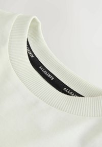 Gros plan sur un col rond côtelé blanc avec une étiquette intérieure noire portant la mention "ALLSAINTS" en texte blanc.