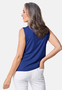 Mouwloze blauwe top van gladde stof, met een ronde zoom en een relaxte pasvorm, gecombineerd met witte broek. Eenvoudig en strak ontwerp.