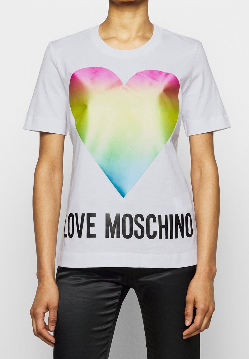 Bílý bavlněný tričko s velkým, barevným srdcovým motivem a výrazným černým textem „LOVE MOSCHINO“ na dolní části.