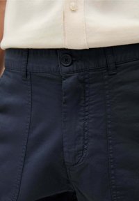 Pantalons en coton bleu marine avec une fermeture à bouton, des poches avant et une texture lisse. Le tissu semble léger avec des détails de couture subtils.