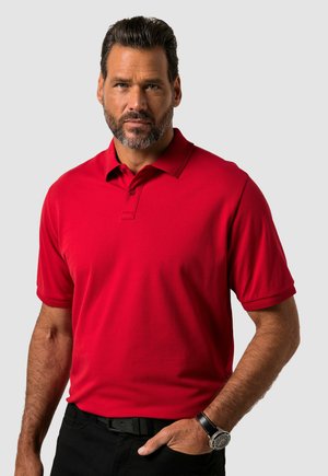Rotes Polohemd mit Kragen, kurzen Ärmeln und einer Knopfleiste mit drei Knöpfen; glattes Material, getragen mit schwarzen Hosen und einer Armbanduhr.