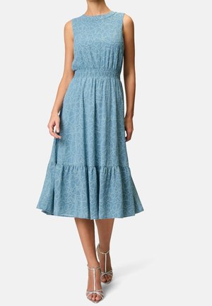 Niebieska sukienka midi bez rękawów z białym kwiatowym wzorem, marszczona w talii, z falbaną u dołu, noszona z srebrnymi sandałami na wysokim obcasie z paskami.