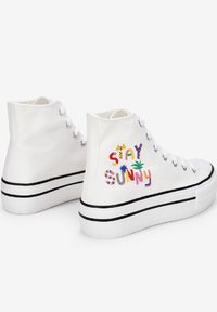 Scarpe alte in canvas bianco con ricamo colorato "STAY SUNNY", suole a strisce nere e occhielli in metallo per i lacci.