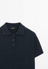 Marineblaues Strick-Poloshirt mit flachem Kragen, kurzen Ärmeln, Zwei-Knopf-Leiste und strukturiertem Stofffinish. Etikett am Kragen sichtbar.