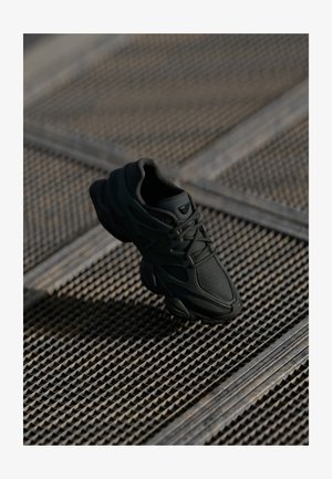 Black athletic shoe made of mesh and synthetic materials, featuring a textured upper, padded collar, and a rubber sole with curved accents.