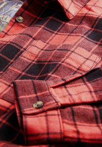 Czerwona i czarna flanelowa koszula w kratę, z detalami w postaci guzików, o miękkiej fakturze i klasycznym fasonie kołnierza. Tkanina ma lekko szczotkowane wykończenie.