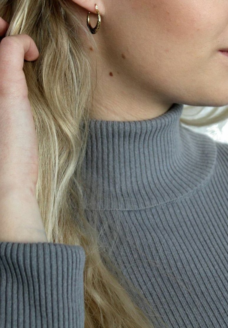 Maglione a collo alto grigio a coste, primo piano sulla zona del collo, presenta una sottile texture. Orecchino a cerchio d'oro piccolo visibile sull'orecchio sinistro.
