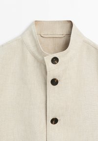 Light beige linen shirt with a stand collar and three dark brown buttons down the front.
