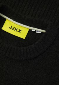 Zwarte trui met een geribbeld decolleté, voorzien van een felgele label met "JJXX" en een crèmekleurige rand. Bevat maat- en herkomstlabels.