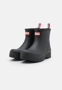 Schwarze, wasserdichte Stiefeletten aus Gummi mit strukturierter Oberfläche, roten und weißen gestreiften Zuglaschen und einem Logo an der Seite.