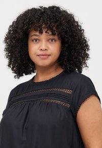 Blusa negra con mangas cortas, rayas texturizadas e inserción de encaje en el escote. Escote redondo con detalle de borde festoneado.