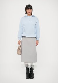 Helehall sinine kapuutsi ja nööriga pusa, hall maxi seelik pitsist äärisega, mustad põlvikud. Käes metallik käekott.