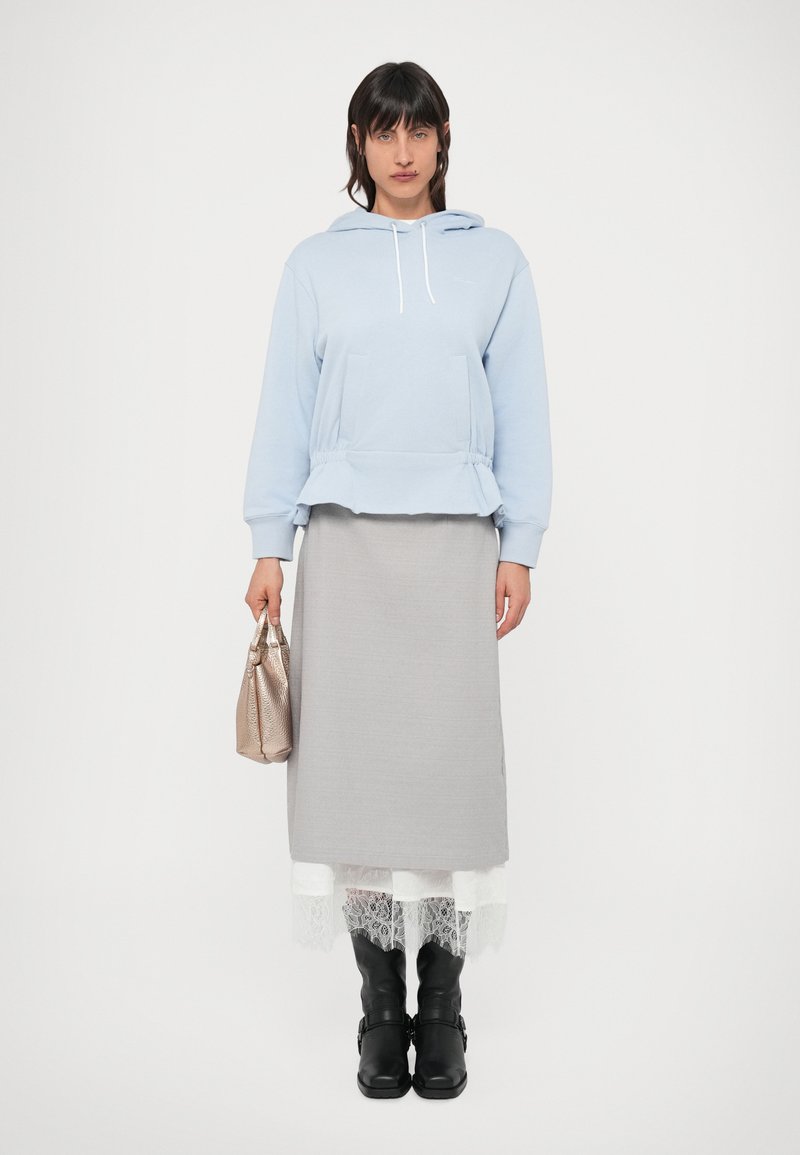 Helehall sinine kapuutsi ja nööriga pusa, hall maxi seelik pitsist äärisega, mustad põlvikud. Käes metallik käekott.