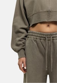 Kort olijfgroen sweatshirt met een rits, gecombineerd met sweatpants met elastische taille. Zachte textuur, ontspannen pasvorm en ribbels aan de mouwen.