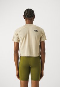 Beige kortärmad t-shirt med korta ärmar, med en svart logotyp på övre ryggen; kombinerad med gröna tajta shorts.