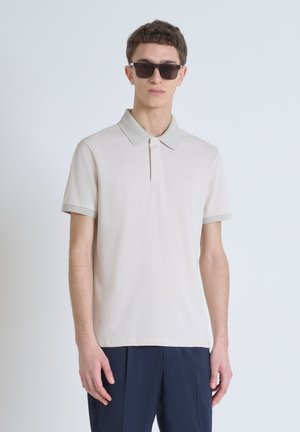 Polo-shirt en beige clair avec un col côtelé et des manches côtelées. Le tissu est lisse, avec un logo subtil sur la poitrine.