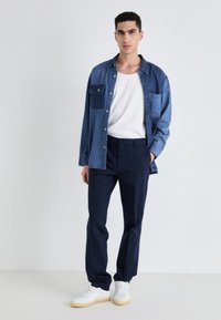 Denim shirt in blue with front pocket, white T-shirt, navy trousers, and white sneakers. Simple design, solid colors, lightweight fabric.