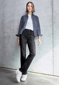 T-shirt azzurro chiaro, camicia di velluto grigio scuro e jeans neri. Sneakers bianche completano l'outfit. Tessuti morbidi e vestibilità casual.