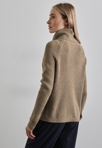 Beige ribbad tröja med hög krage, med en texturerad stickad design. Plagget har en figurnära silhuett och långa ärmar.