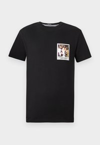 Black cotton t-shirt featuring a rectangular graphic patch on the left chest with a photo and text in a white border.