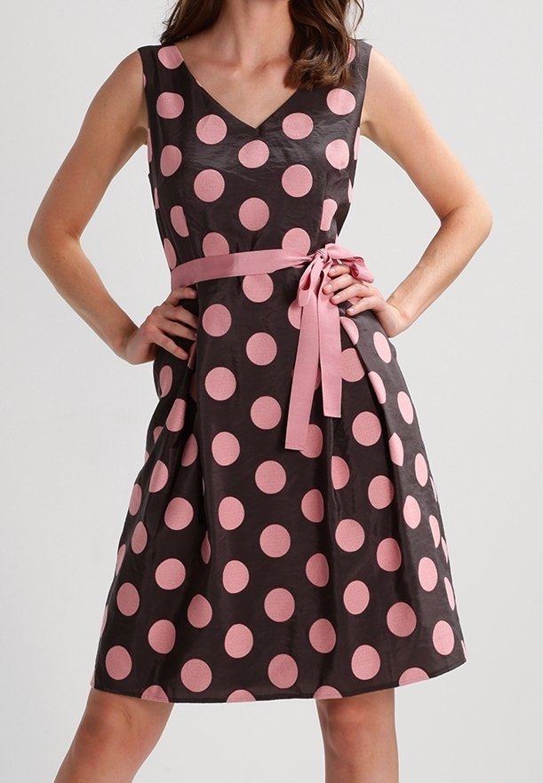 Vestido negro con grandes lunares rosas, escote en V y un lazo rosa en la cintura. Hecho de una tela suave con una falda acampanada y diseño sin mangas.