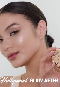 Compact de surligneur avec un design étoilé et des accents dorés, tenu par une personne avec une peau éclatante, mettant en valeur une texture lisse et un éclat subtil.
