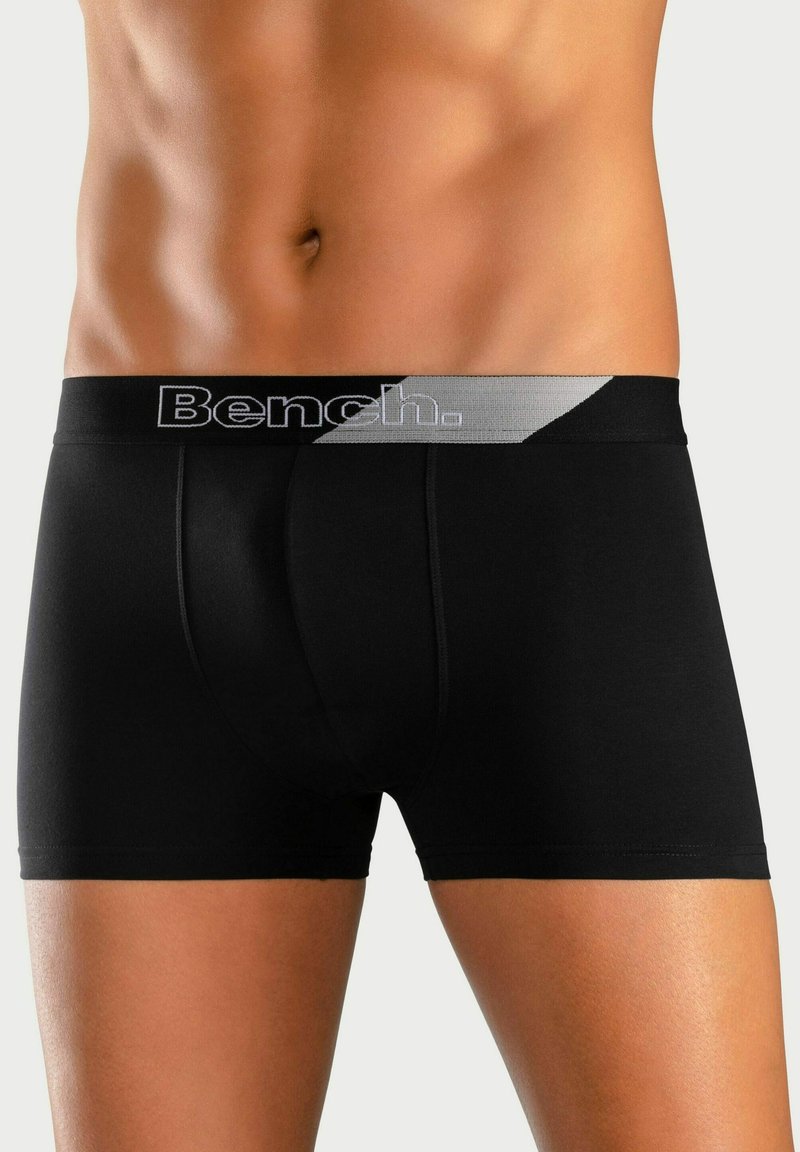 Black boxer briefs with a grey elastic waistband featuring "Bench." logo, smooth fabric, and a fitted design contouring the body shape.
