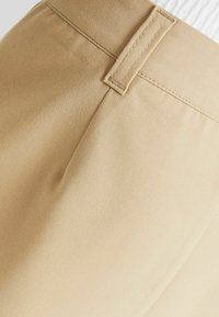 Pantalon beige sur mesure avec une texture lisse, doté d'une poche arrière unique, de coutures finement réalisées et d'une ceinture plate.