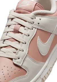 Sneaker Nike en cuir et textile, principalement rose clair et crème, avec des perforations prononcées et le logo swoosh classique.